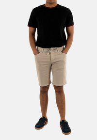 T-shirt nera con rifiniture rosse, pantaloni beige chiaro con cordino, e scarpe da ginnastica blu navy con dettagli marroni. Outfit casual esposto.