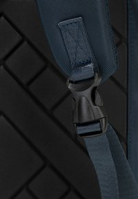 Sangle en nylon bleu marine avec une boucle en plastique noir. Fond texturé avec un motif géométrique de losanges en relief. Conception durable axée sur la robustesse.