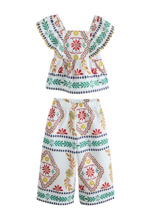 Két részes fehér öltözet széles szárú nadrággal és fodros ujjú felsővel, színes virágos és geometriai mintákkal díszítve.