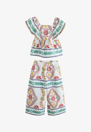 Dvojdielny biely outfit so širokými nohavicami a topom s volánovými rukávmi, zdobený farebnými kvetinovými a geometrickými vzormi.