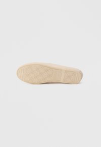 Μπεζ αθλητικό παπούτσι με λαστιχένια σόλα που διαθέτει υφή και σχέδιο. Η εξωτερική σόλα φέρει λογότυπο και ετικέτα μεγέθους, με ομαλή επιφάνεια στην κορυφή.