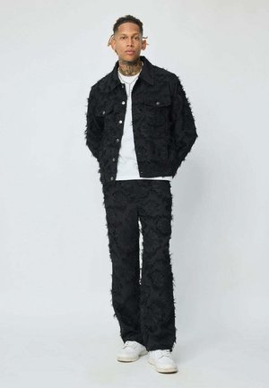 Veste en denim noir et pantalon avec un motif floral texturé, portant un t-shirt blanc en dessous et des baskets blanches.