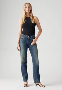 Top din material ribbed, de culoare neagră, asortat cu blugi drepți din denim albastru; blugii au un design standard cu cinci buzunare și o ușoară decolorare.
