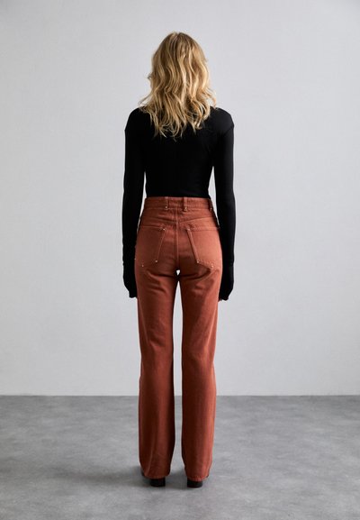 Zwarte lange mouwen top, gecombineerd met rust-oranje hoge taille wijduitlopende broek met achterzakken en subtiele stiksels.