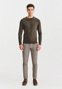 Oliwkowy sweter dzianinowy z okrągłym dekoltem, w zestawieniu z jasnoszarymi spodniami o slim fit i brązowymi butami wsuwanymi. Prosty i dopasowany krój.