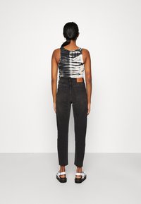 Top sin mangas de teñido anudado negro, pantalones negros de tiro alto con bolsillos traseros, y sandalias blancas con suela negra. Diseño minimalista, silueta ajustada.