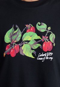 Černé tričko s barevným grafickým motivem červeného ovoce a zelených listů. Bíly nápis "Carhartt WIP Cream of the crop."