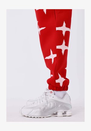 Rode sweatpants met witte sterrenpatronen en elastische boorden, gecombineerd met witte Nike sneakers met zilveren accenten en een textuurachtige zool.