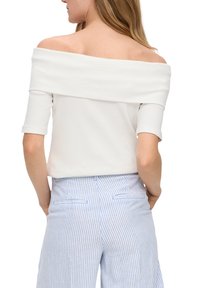 Witte off-the-shoulder top met korte mouwen en geribbelde textuur. Gecombineerd met blauw-witte gestreepte broek met achterzakken.