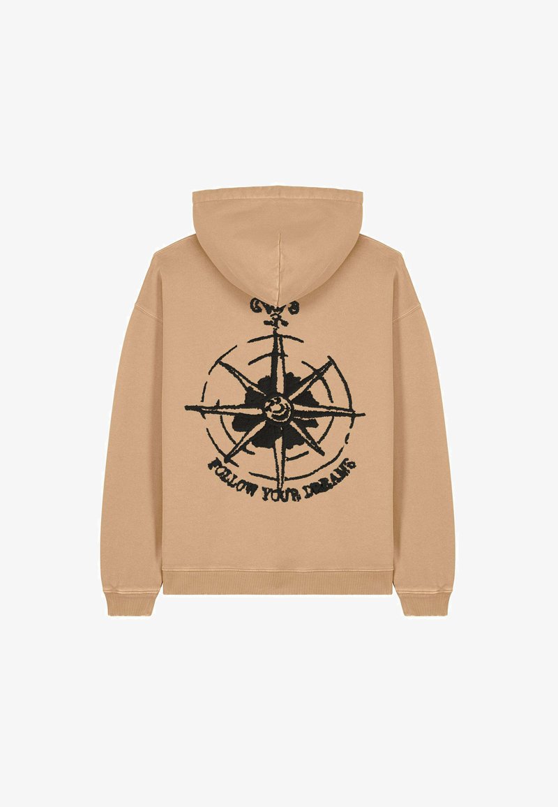 Sweat-shirt beige avec un graphique de boussole noire et le texte "SUIVEZ VOS RÊVES." Conçu avec une capuche à cordon de serrage et des manches côtelées.