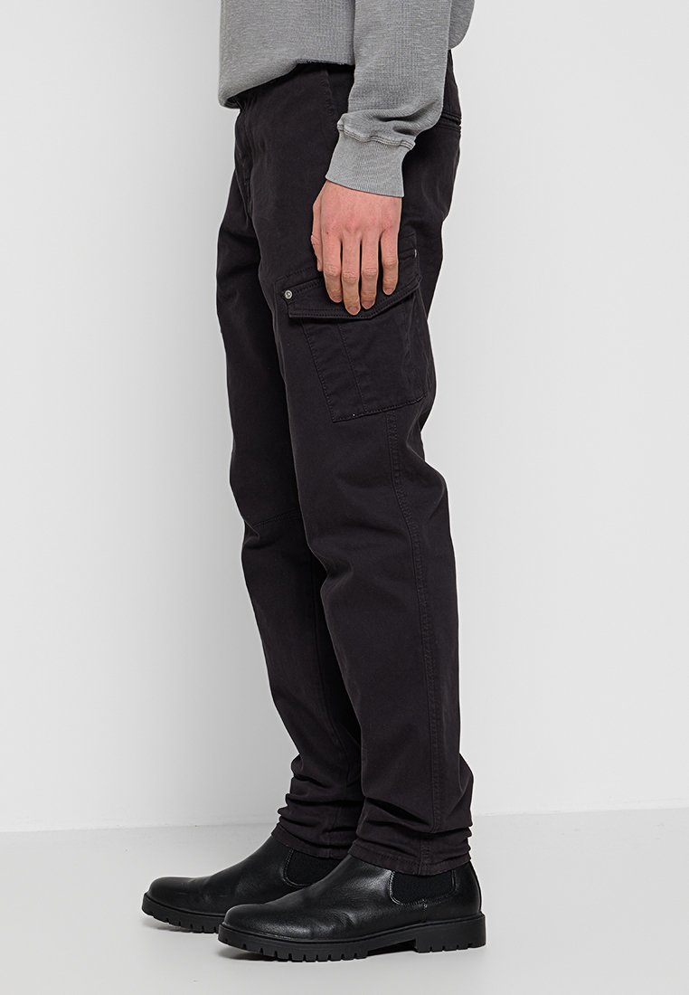 Zwarte cargobroek met een relaxte pasvorm, voorzien van zijzakken en een zachte katoenmix stof. Gemaakt met zwarte enkellaarsjes en een grijze trui.