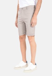 Pantaloni corti grigio chiaro realizzati in tessuto leggero, con chiusura a bottoni e orli risvoltati. Abbinati a sneakers bianche con dettagli beige.