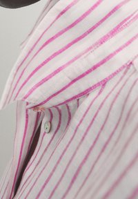 Collet et haut de la poitrine d'une chemise blanche à rayures verticales roses, montrant des boutons et une partie de l'encolure.