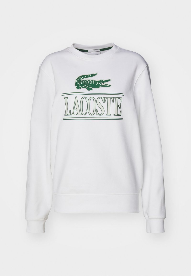 Sudadera blanca con un logo de cocodrilo verde y texto "LACOSTE". Mangas largas, cuello redondo y textura suave y lisa.