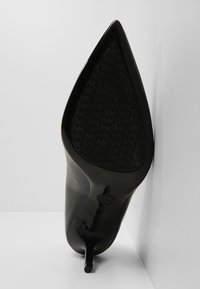 Chaussure à talon haut noire à bout pointu avec semelle texturée présentant un motif répété de logo "MK".