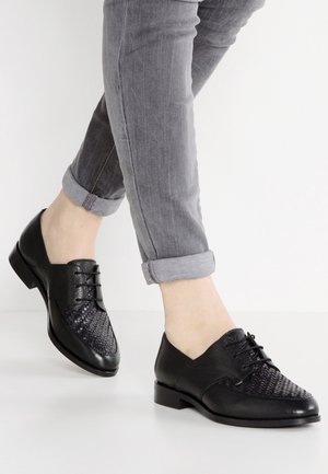 Zwarte leren schoenen met gevlochten details op de neus, platte hak en vetersluiting. Draag met opgerolde grijze jeans.