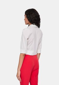 Camicetta bianca cropped con maniche corte e colletto, abbinata a pantaloni rossi a vita alta. Tessuto liscio con dettagli minimi.