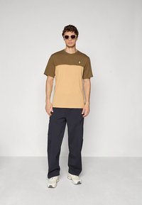 Kortermet t-skjorte med en brun øvre del og beige nedre del, kombinert med mørke cargobukser og hvite sneakers.