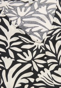 Svartvit blommönstrad tyg med V-ringning, som har böjda former och varierande bladmotiv. Mjuk, texturerad bomullsmaterial.