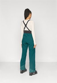 Αδιάβροχες τιρκουάζ σκιές με ρυθμιζόμενους μαύρους ιμάντες, φαρδιά πόδια και πλευρικούς φερμουάρ. Διαθέτουν λείο υφή και ανθεκτικό ύφασμα.