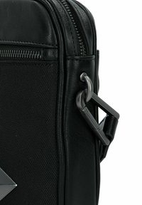 Borsa nera con superficie texturizzata, zip laterale e un dettaglio metallico con gancio a moschettone per il fissaggio. Design compatto e strutturato.