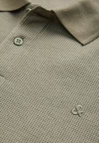 Μπεζ πολο μπλούζα με υφή, γιακά με κουμπιά και μικρό κεντημένο λογότυπο στο στήθος.