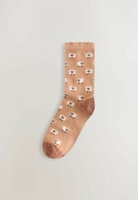 Beige sok met een herhaald patroon van witte schapen met bruine accenten, weergegeven tegen een lichte achtergrond.