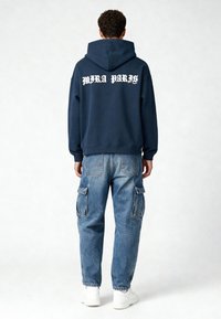 Marineblauwe hoodie met "MIRA PARIS" in het wit op de achterkant, gecombineerd met lichtblauwe cargojoggingbroeken met meerdere zakken.