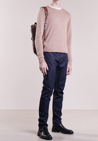 Bežový svetr, úzké tmavé džíny, černé kotníkové boty. Hnědý kožený batoh se strapcem. Jednoduchý design, neutrální barvy a strukturovaná tkanina.