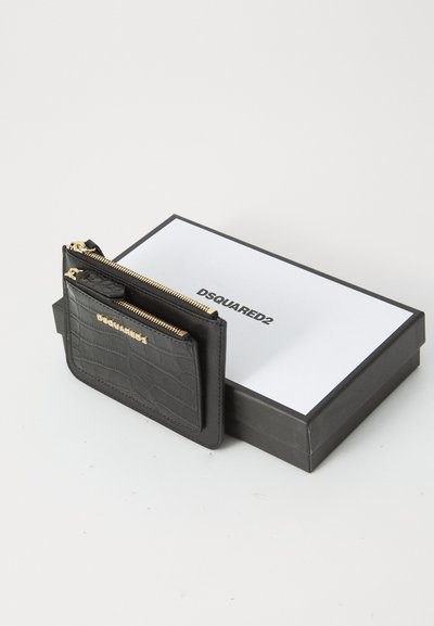 Porte-cartes en cuir noir à texture crocodile avec des zippers dorés et le logo DSQUARED2, posé sur une boîte DSQUARED2 noire et blanche.