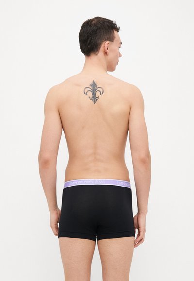 Boxers noirs avec une ceinture violette portant le logo "Emporio Armani", en tissu lisse et à la coupe ajustée sur un torse nu.