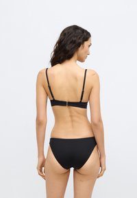 Μαύρο σετ μπικίνι με μίνιμαλ σχεδιασμό, λεπτές ρυθμιζόμενες τιράντες και ασφαλές κούμπωμα στο πίσω μέρος. Λείο, ελαστικό ύφασμα και κλασική κοπή.