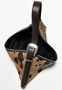Brun och svart prickig tygväska med triangulärt mönster; har en brun läderrem och silverdetaljer med dragkedjestängning.
