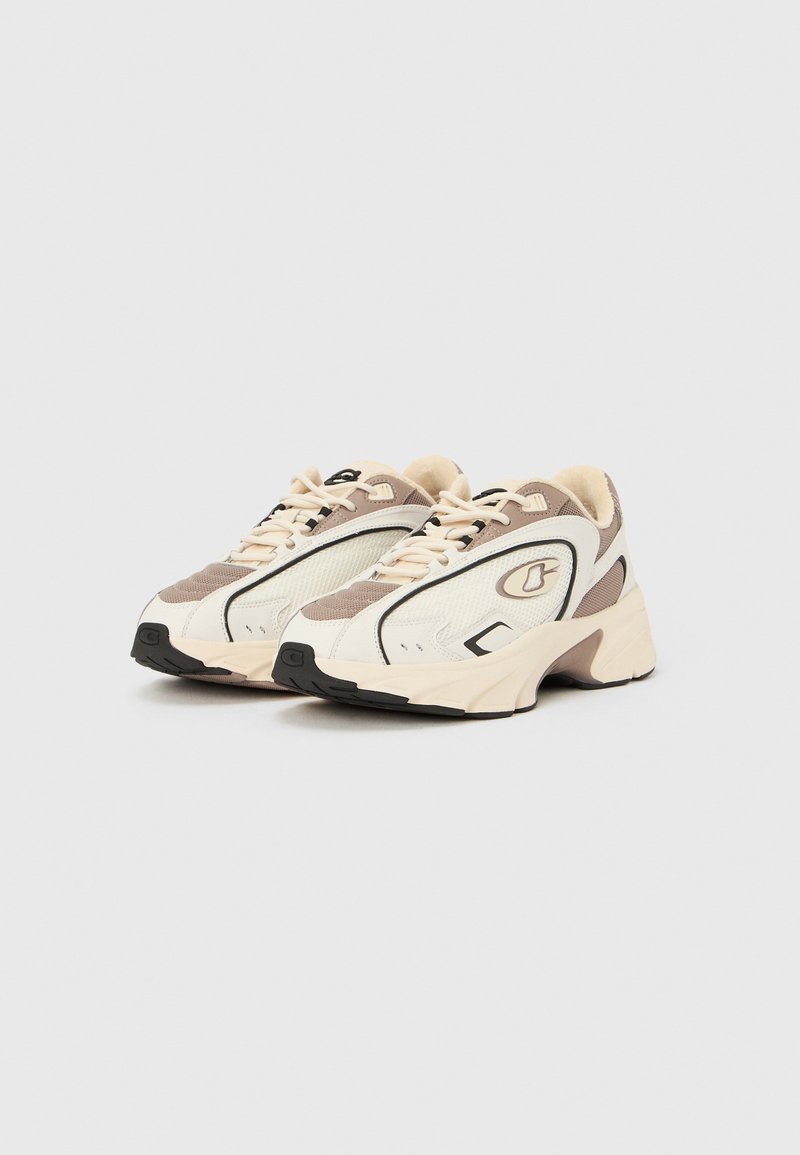 White and beige sneakers with mesh, leather, and rubber materials. Features black accents, rounded toe, and textured sole.