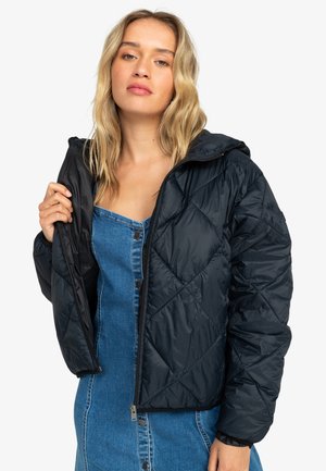 Black quilted puffer jacket with a hood, featuring a zipper closure and elastic cuffs, worn over a denim dress.