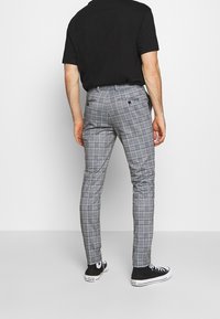 Grå rutiga byxor med slim fit, med platt framdel, två bakfickor och en slät tygtextur. Matchas med svarta sneakers.