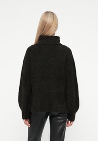 Übergroßer dunkelbrauner Pullover mit hohem Kragen, strukturiertem Stoff und langen Ärmeln, kombiniert mit schwarz fitting Hosen.