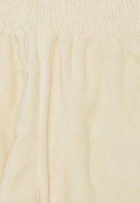 Tissu couleur crème avec une surface douce et texturée et une taille élastique. Le matériau semble moelleux et légèrement réfléchissant.