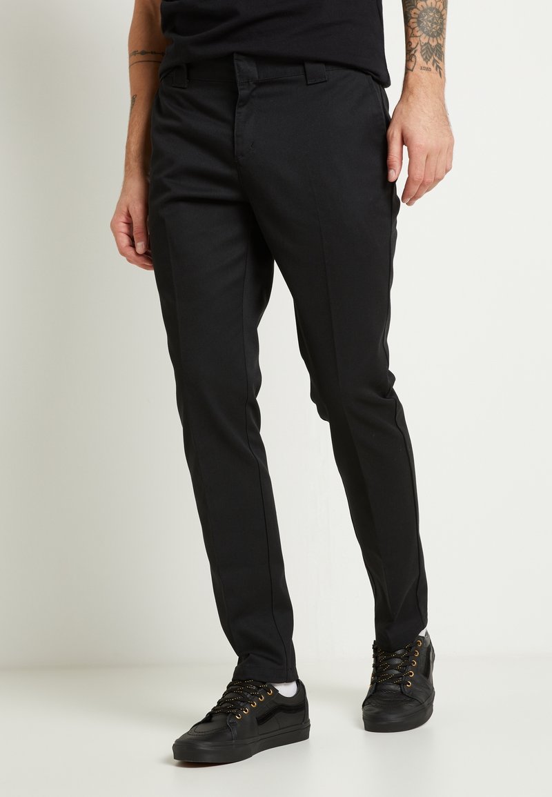 Černé kalhoty na míru, slim fit, s hladkou texturou. Mají boční kapsy, nošeny s černými teniskami a černou košilí.