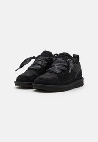 Des baskets noires présentant un mélange de matériaux en daim et en maille, avec des accents texturés et une semelle en caoutchouc épaisse. Les lacets sont présentés dans un motif complexe.
