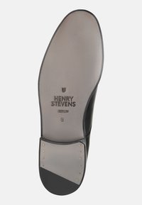 Schwarze Ledersohle mit eingeprägtem Markennamen "Henry Stevens" und "Berlin." Verziert mit goldenen Nieten und einer glatten, grauen Oberfläche.