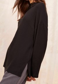 Mustissa pitkähihainen paita, jossa on rento leikkaus. Paidan korkea kaula-aukko ja sivuhalkiot ovat tyylikkäitä yksityiskohtia, ja se on valmistettu pehmeästä, tekstuurista kankaasta.