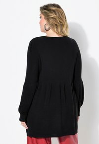 Maglione nero lavorato a maglia con design peplum, maniche lunghe a sbuffo e texture a coste, caratterizzato da un colletto rotondo e spacchi laterali.