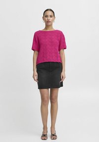 Fukšijas krāsas adīta blūze ar rakstainu tekstūru un īsām piedurknēm; kombinēta ar melnu džinsu svārku un striķu sānīšiem.