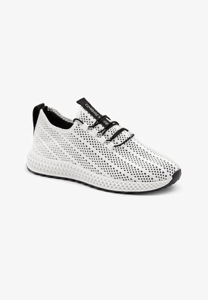 Baskets blanches en maille respirante avec lacets élastiques noirs, languette de talon noire et semelle blanche texturée, montrées sous un léger angle.