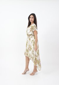 Asymmetrisk vit klänning med grönt och brunt blommönster, mjukt tyg, korta svävande ärmar, insnörad midja, matchad med klackar med genomskinliga remmar.