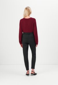 Burgunder strikket sweater med lange ærmer, kombineret med sorte stribede bukser og sorte hæle. Outfittet vises fra ryggen.