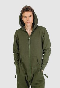 Olijf groene zip-up onesie met een capuchon, gemaakt van zachte stof. Heeft voorzakken en verstelbare manchetten. Subtiel geborduurd logo op de zak.