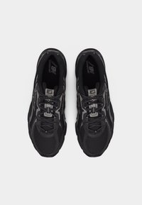 Par de zapatillas de correr New Balance negras con parte superior de malla y detalle de cordones, vistas desde arriba sobre un fondo blanco.