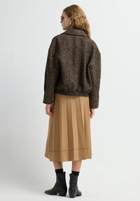 Bruine visgraatjasje, beige geplooide rok, zwarte enkellaarsjes. Gelaagde stof met een kraag, getailleerde taille en subtiele stikdetails.